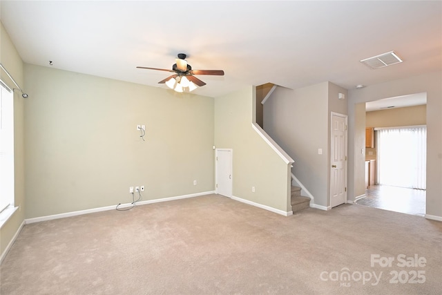 carpeted empty room with a ceiling fan, visible vents, stairway, and baseboards