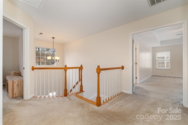 hallway with visible vents, baseboards, carpet, a chandelier, and an upstairs landing