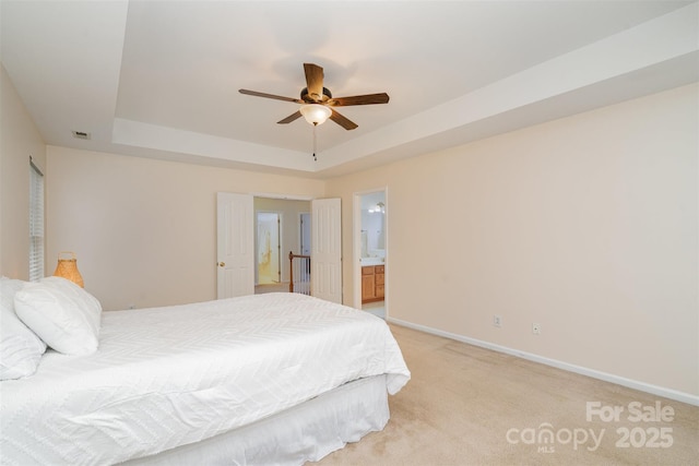 bedroom featuring a tray ceiling, baseboards, light colored carpet, and ensuite bath