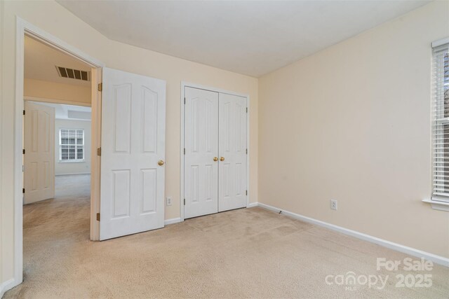 unfurnished bedroom featuring baseboards, visible vents, a closet, and light carpet