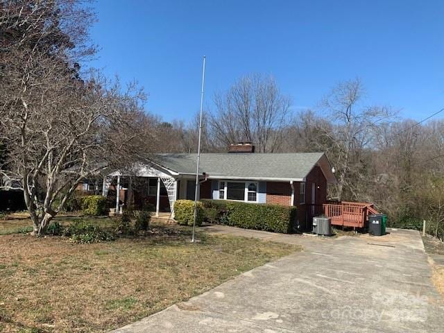 ranch-style home featuring a front lawn, a chimney, a wooden deck, and central air condition unit