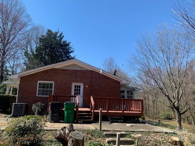 back of property with central AC, brick siding, and a wooden deck