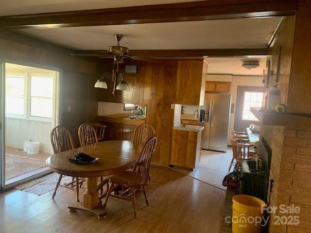 dining room with ceiling fan, light wood-style flooring, wooden walls, a fireplace, and beam ceiling