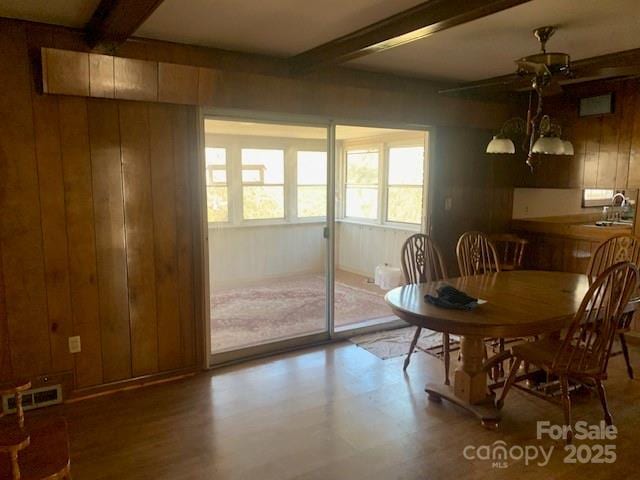 dining room featuring wooden walls, visible vents, a chandelier, and beam ceiling