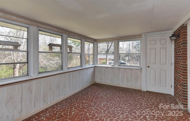 unfurnished sunroom featuring baseboards, wood walls, and a wealth of natural light