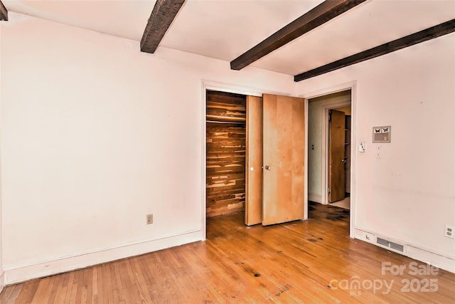 unfurnished bedroom featuring visible vents, beamed ceiling, a closet, light wood-style floors, and baseboards