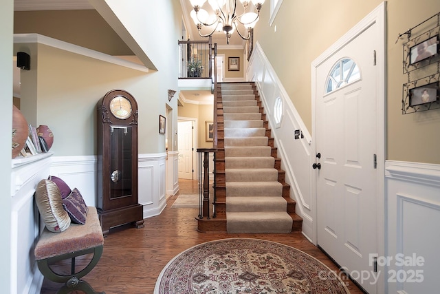 entryway with a notable chandelier, a towering ceiling, ornamental molding, wainscoting, and dark wood finished floors