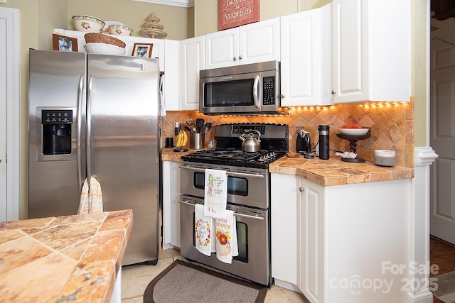 kitchen with tile countertops, stainless steel appliances, tasteful backsplash, and white cabinetry