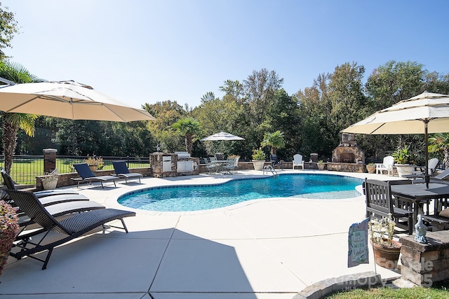 view of pool featuring an outdoor fireplace, fence, exterior kitchen, a fenced in pool, and a patio area