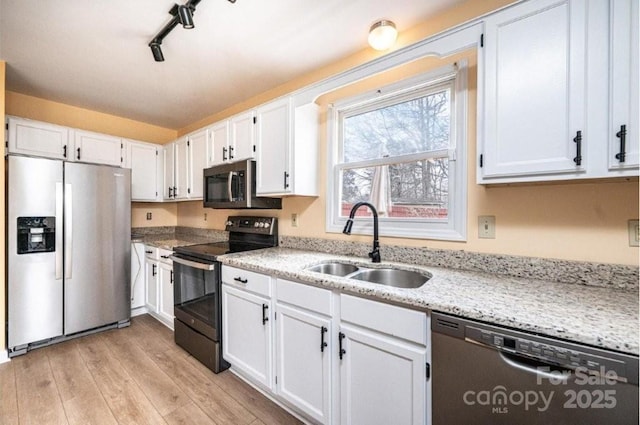 kitchen featuring light wood-style flooring, light stone counters, stainless steel appliances, white cabinetry, and a sink