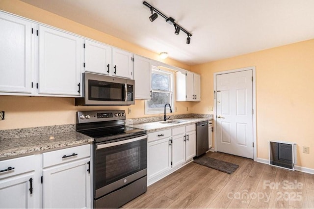 kitchen with stainless steel appliances, white cabinets, a sink, and light wood-style flooring