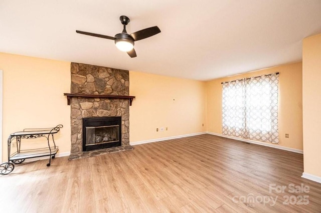 unfurnished living room featuring a stone fireplace, wood finished floors, a ceiling fan, and baseboards