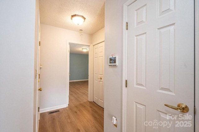 hall with baseboards, visible vents, a textured ceiling, and light wood finished floors