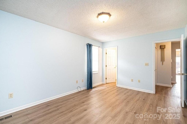 unfurnished room featuring a healthy amount of sunlight, light wood-style flooring, visible vents, and baseboards