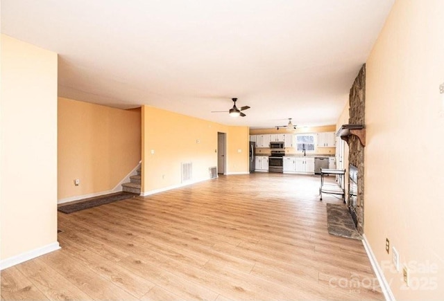 unfurnished living room with visible vents, light wood-style flooring, stairway, a ceiling fan, and baseboards