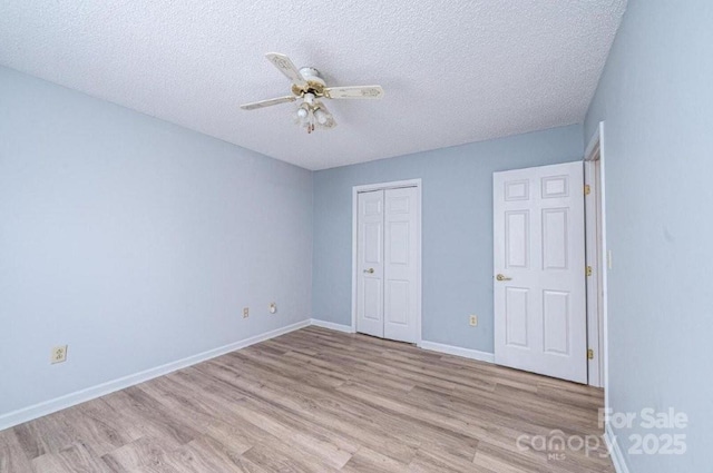 unfurnished bedroom with a closet, light wood-style flooring, ceiling fan, a textured ceiling, and baseboards