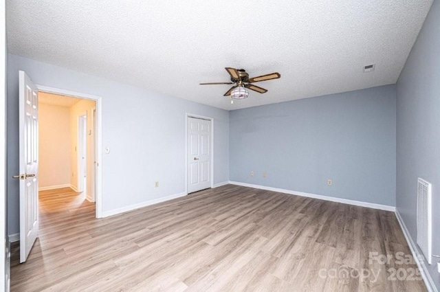 unfurnished room with light wood finished floors, visible vents, baseboards, and a textured ceiling