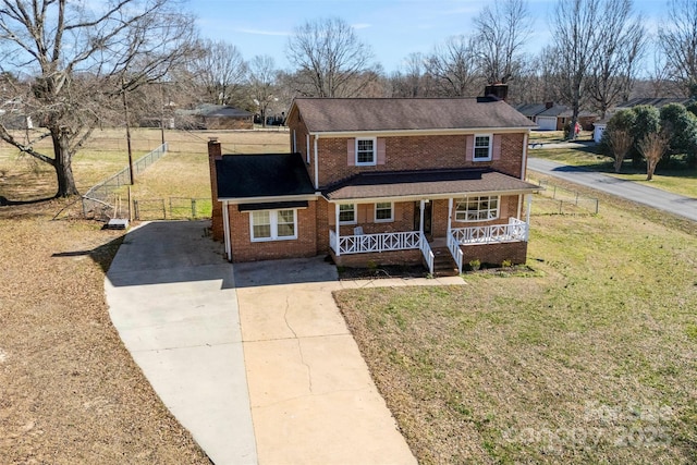 traditional-style house featuring brick siding, a chimney, a porch, driveway, and a front lawn