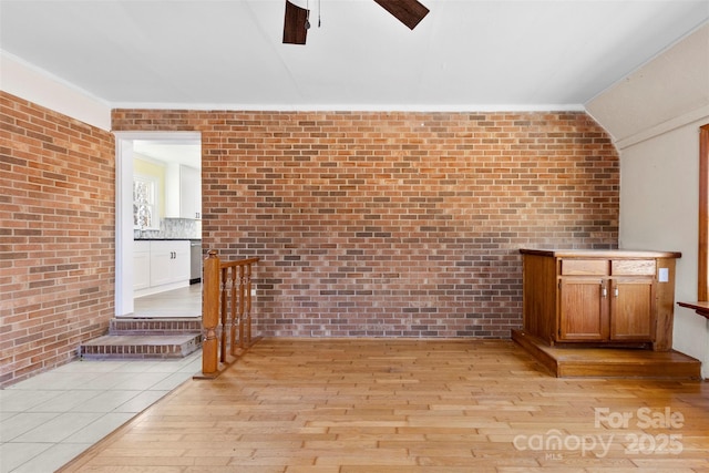 unfurnished living room with vaulted ceiling, brick wall, and light wood-type flooring