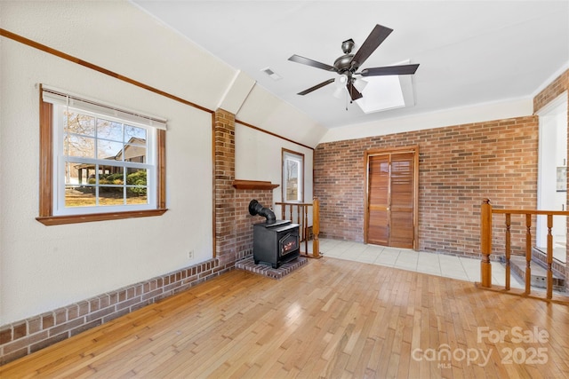 unfurnished living room with plenty of natural light, visible vents, hardwood / wood-style flooring, a wood stove, and vaulted ceiling