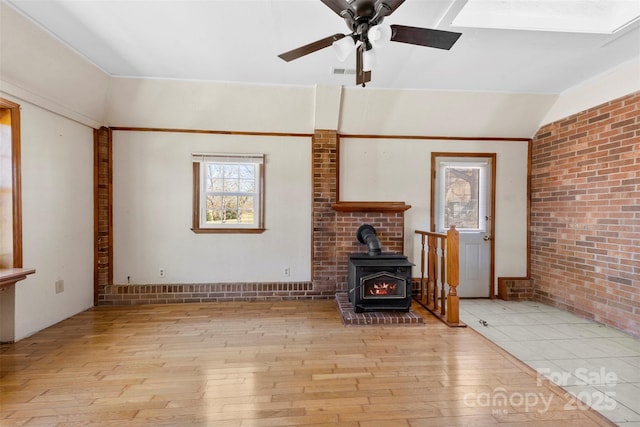 unfurnished living room featuring lofted ceiling, brick wall, a wood stove, and light wood-style floors