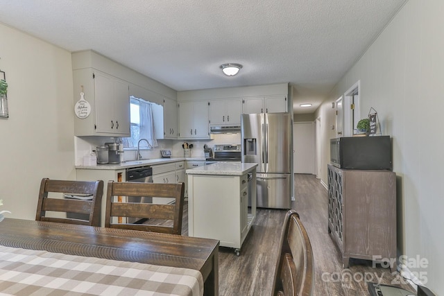 kitchen with a center island, under cabinet range hood, light countertops, appliances with stainless steel finishes, and a sink