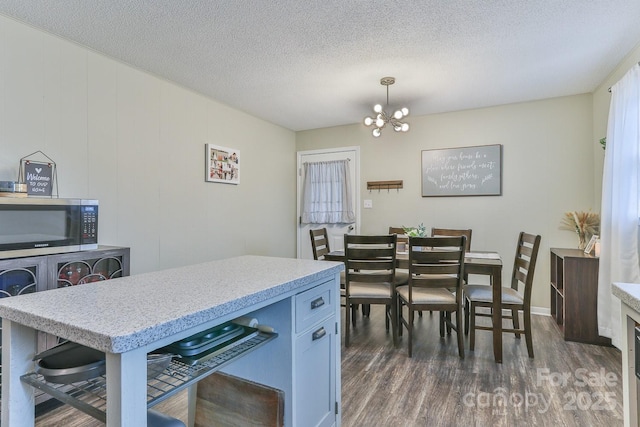 kitchen with a textured ceiling, an inviting chandelier, dark wood-type flooring, pendant lighting, and stainless steel microwave