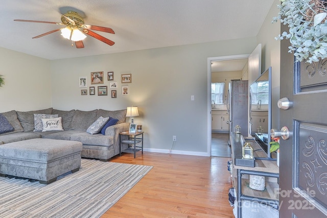 living area with light wood-type flooring, baseboards, and ceiling fan