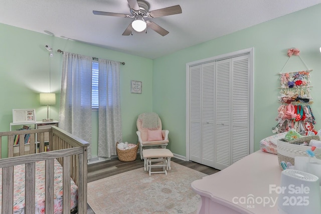 bedroom featuring a crib, wood finished floors, a closet, and a ceiling fan