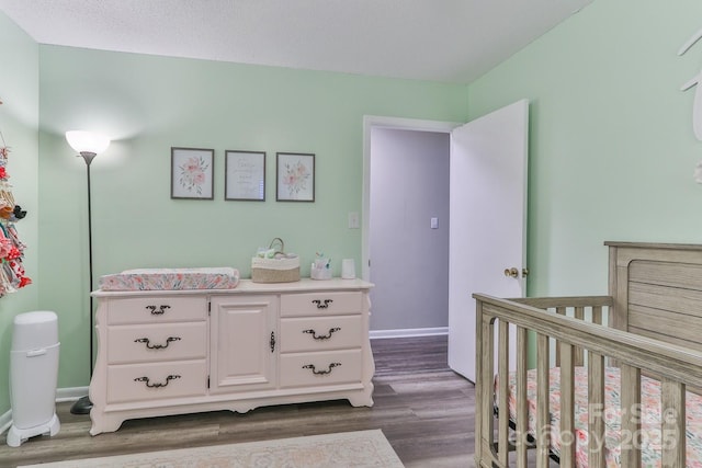 bedroom with dark wood finished floors, baseboards, and a nursery area