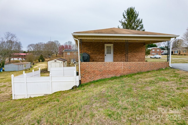 view of side of property featuring brick siding, fence, a yard, an outbuilding, and a storage unit