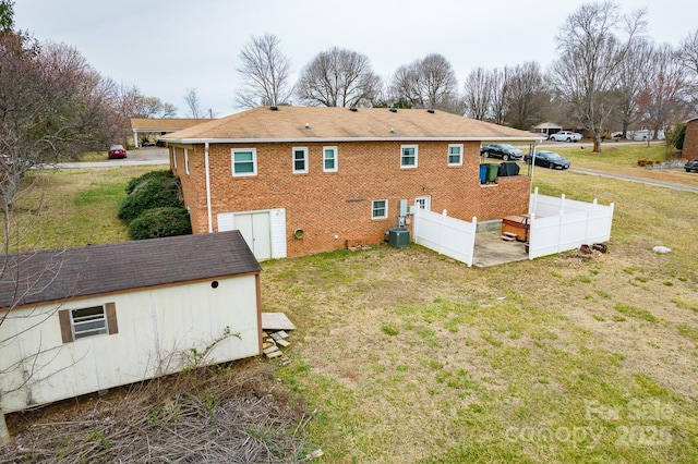 rear view of house with brick siding, central air condition unit, a lawn, and fence