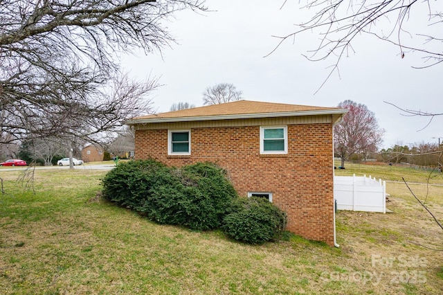 view of property exterior with a lawn, brick siding, and fence