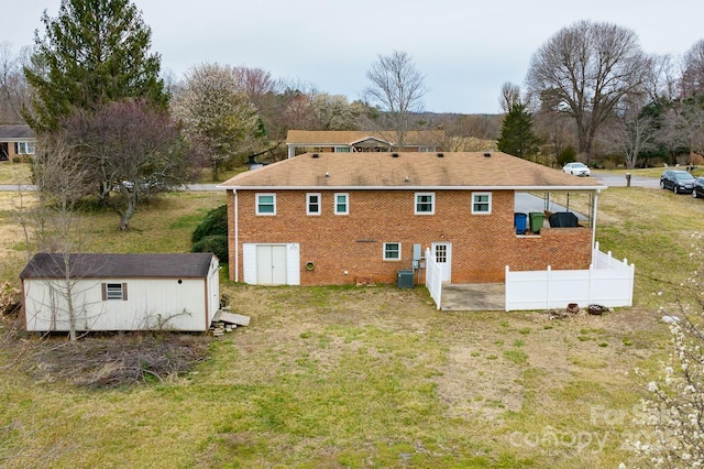 back of property with an outbuilding, brick siding, a lawn, and fence