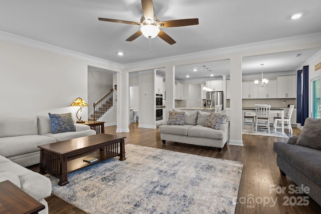 living room with stairway, dark wood-type flooring, ceiling fan with notable chandelier, crown molding, and recessed lighting