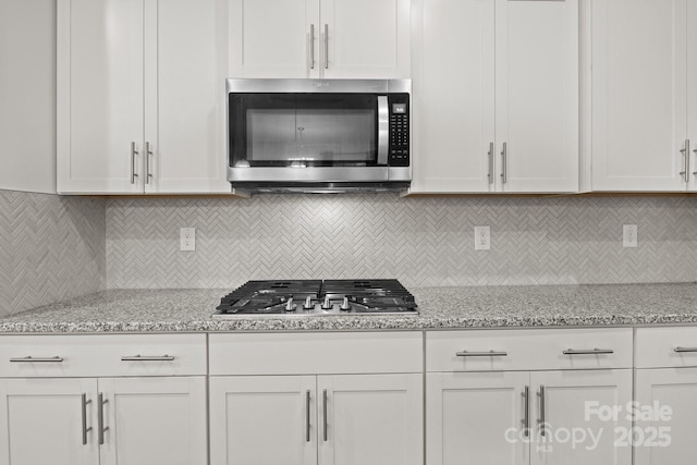 kitchen featuring light stone countertops, appliances with stainless steel finishes, white cabinets, and decorative backsplash