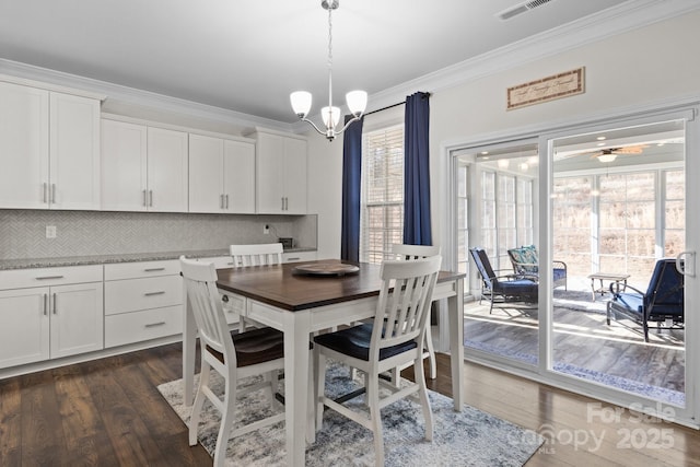 dining space with dark wood-type flooring, an inviting chandelier, visible vents, and crown molding