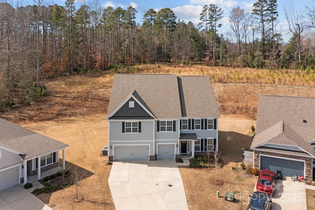 view of front facade featuring a garage, driveway, roof with shingles, a forest view, and board and batten siding