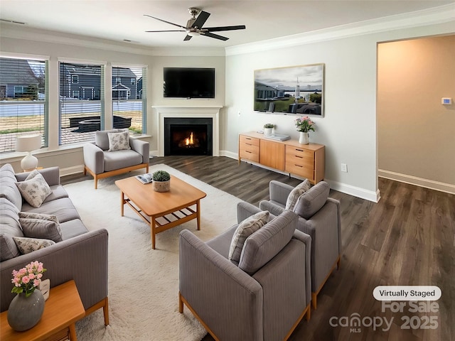 living room featuring crown molding, a ceiling fan, wood finished floors, a warm lit fireplace, and baseboards