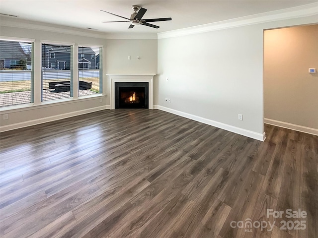 unfurnished living room with a warm lit fireplace, ceiling fan, baseboards, ornamental molding, and dark wood finished floors