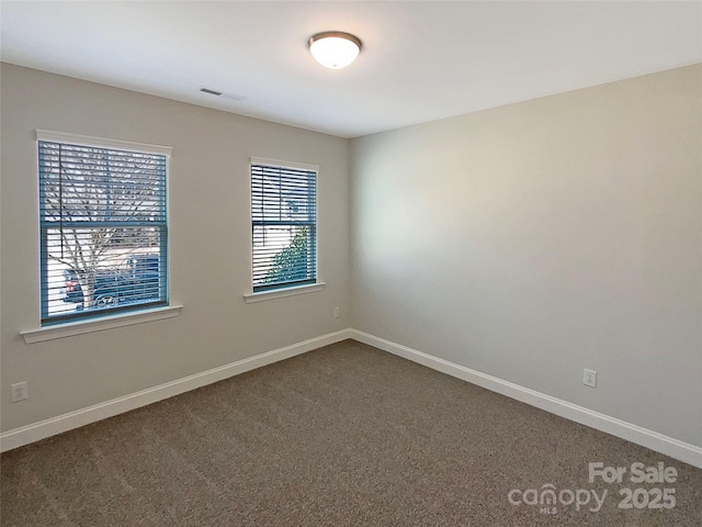 empty room featuring baseboards, visible vents, and dark carpet