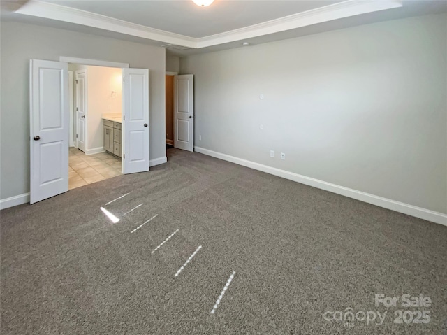 unfurnished bedroom with light carpet, a raised ceiling, connected bathroom, and baseboards