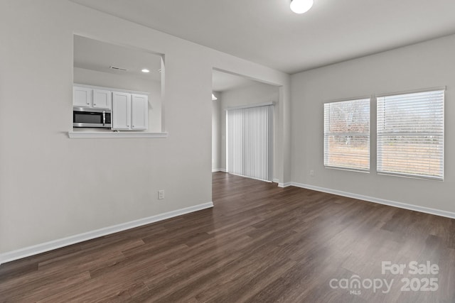 unfurnished living room featuring dark wood-style flooring and baseboards