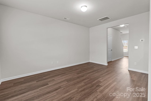 empty room featuring dark wood-style flooring, visible vents, and baseboards