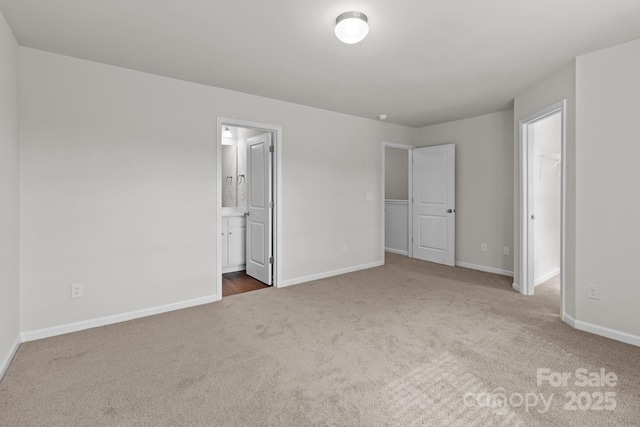 unfurnished bedroom with a spacious closet, carpet floors, ensuite bath, and baseboards