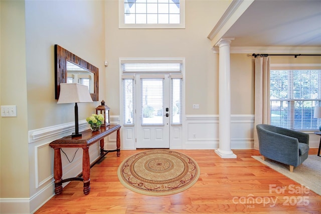 foyer featuring ornate columns, a wainscoted wall, and light wood-type flooring