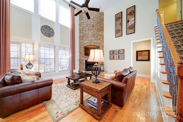 living room with light wood-style floors, a ceiling fan, a stone fireplace, and a towering ceiling