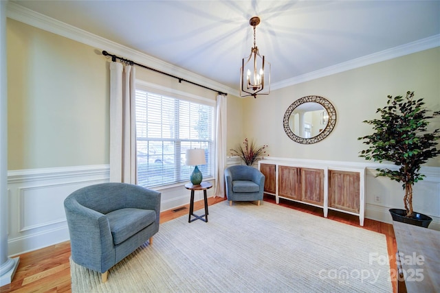 sitting room with an inviting chandelier, wainscoting, crown molding, and wood finished floors