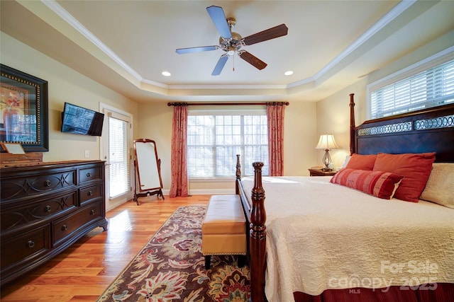 bedroom featuring light wood-style floors, a raised ceiling, and crown molding