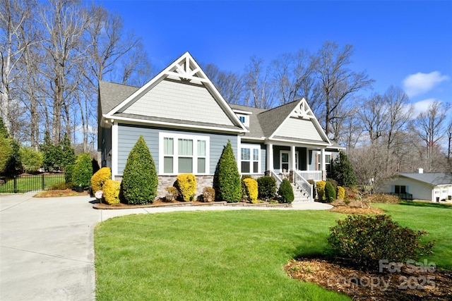 view of front of home featuring stone siding, fence, covered porch, and a front yard